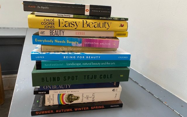 A stack of books on the subject of beauty. White background, grey tabletop.