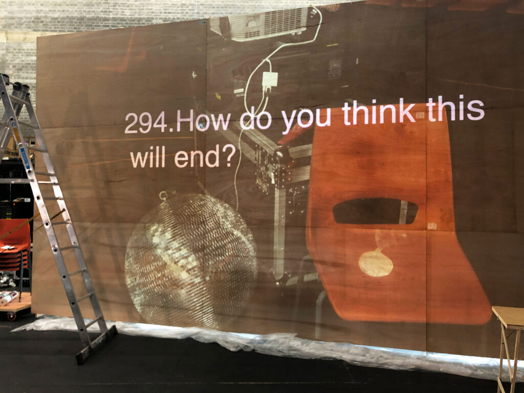 A screen with a photo of a disco ball and an orange chair, with a question overtop that reads '294. How do you think this will end?'
