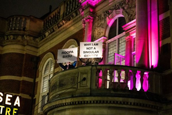 Two people hold signs from BAC's balcony: Roopa Basu Why I am not a singular identity