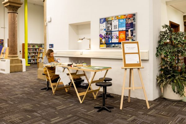 Artist Kate Daley sits at a table of bookbinding materials in Leeds Central Library