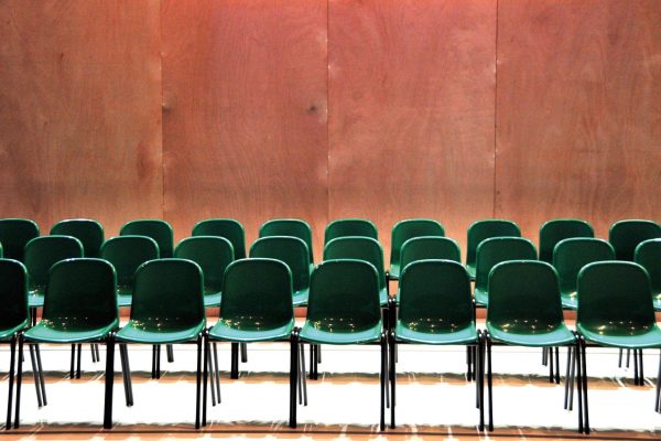 Wooden panelled wall at the back with 3 rows of green plastic chairs in the foreground
