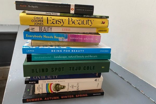 A stack of books on the subject of beauty. White background, grey tabletop.